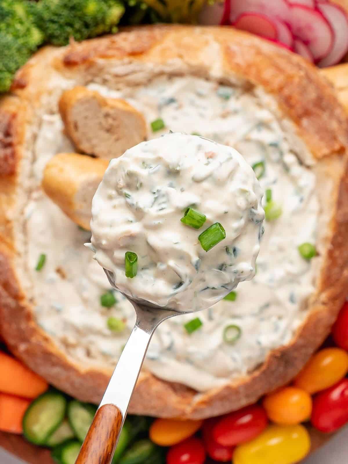 Spoon scooping out spinach dip from a bread bowl underneath.