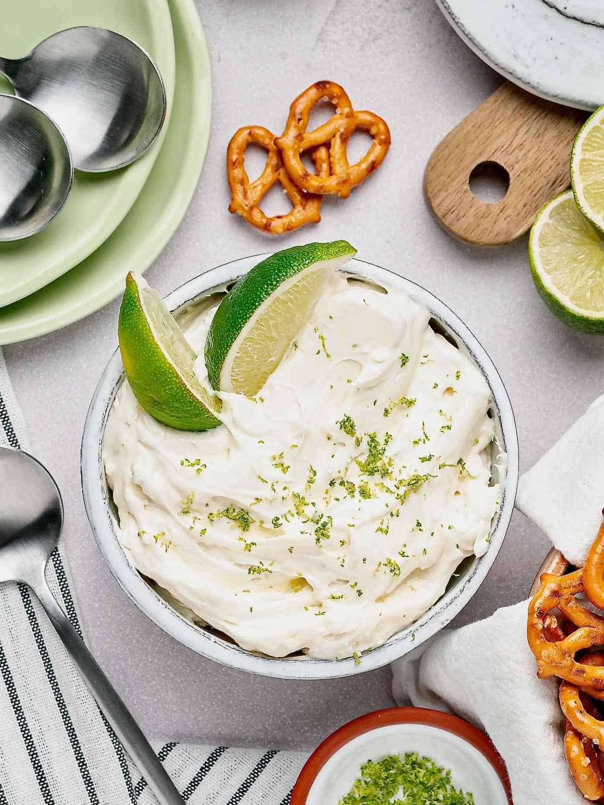 White bowl of margarita dip with lime wedges.