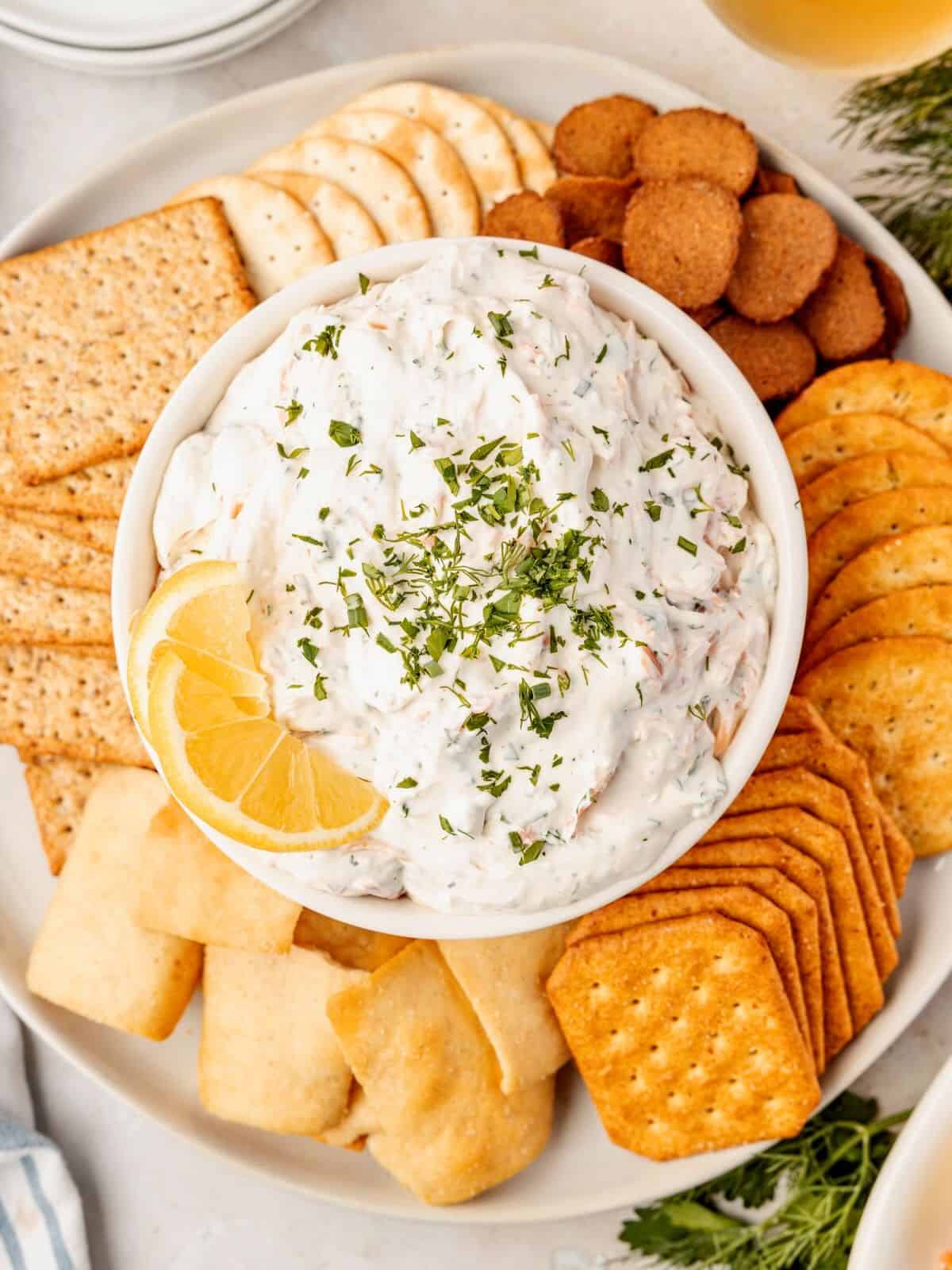 Lemon in a bowl of smoked salmon dip surrounded by assorted dippers.