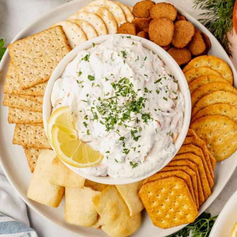 Smoked salmon dip in a white bowl surrounded by crackers with a lemon.