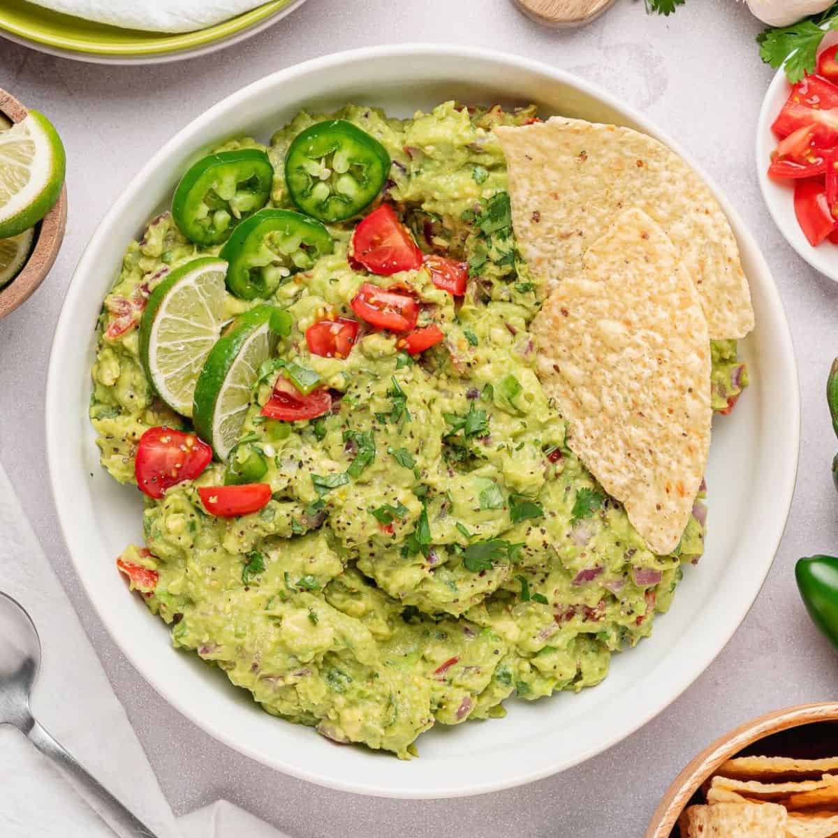 Large bowl of guacamole with jalapeño peppers, lime, onions and tomatoes.
