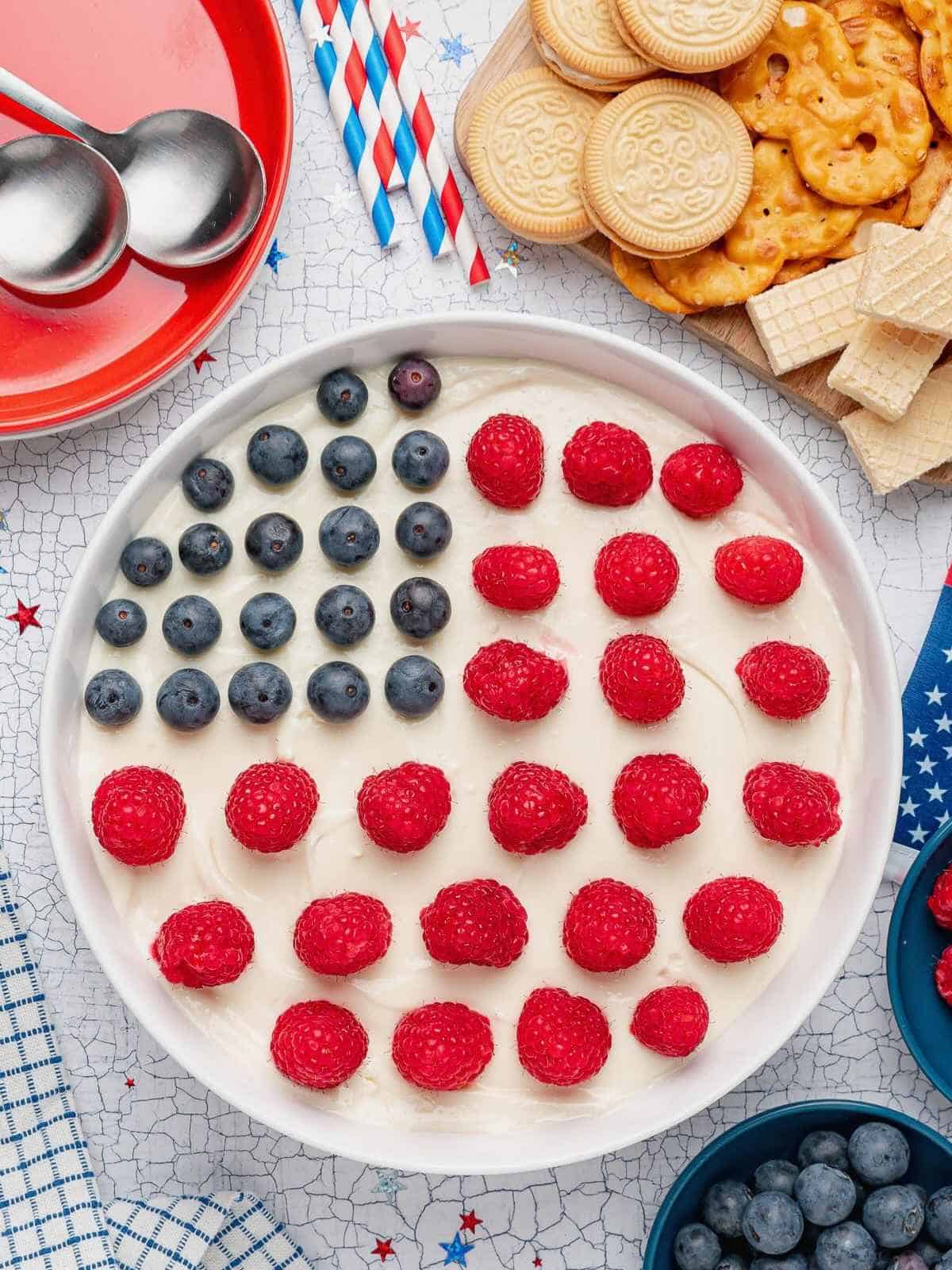 Overhead photo of American Flag Dessert Dip in a white bowl surrounded by cookies.