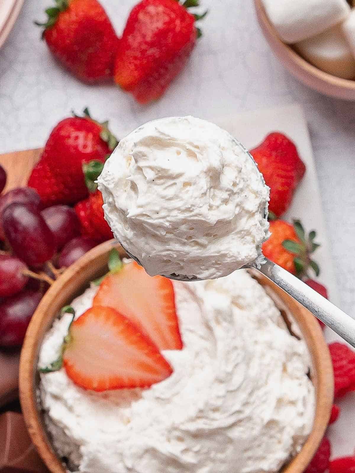 Spoonful of whipped marshmallow fruit dip lifted above a bowl.