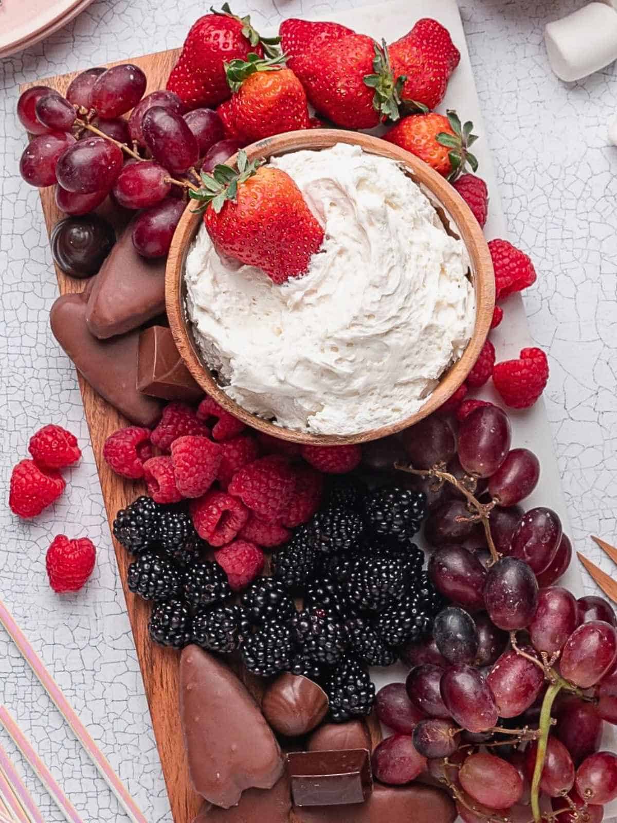 Dessert Dip Board with fruit dip surrounded by berries and chocolate.