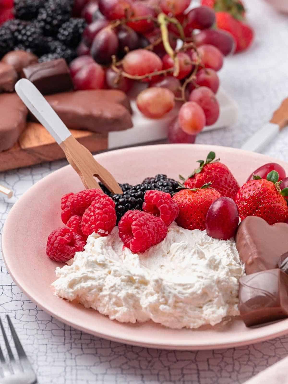 Marshmallow fruit dip on a plate with berries and chocolate.