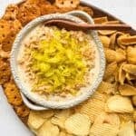 Mississippi Pot Roast Dip in a white bowl surrounded by pretzel crisps, potato chips and Fritos.