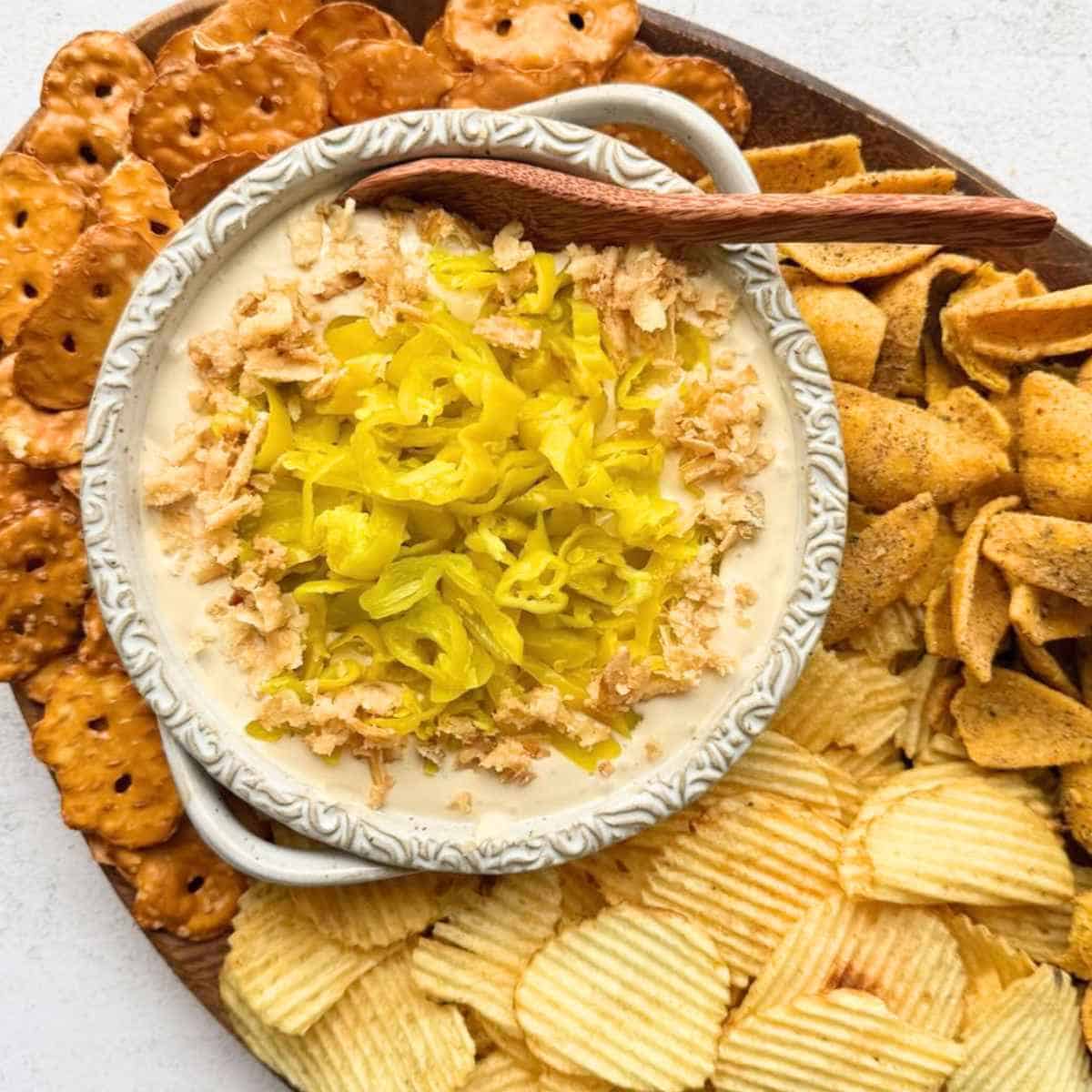 Mississippi Pot Roast Dip in a white bowl surrounded by pretzel crisps, potato chips and Fritos.