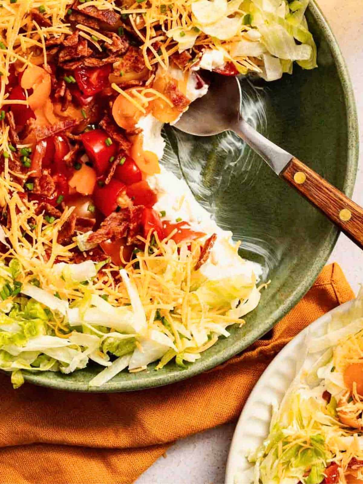 BLT Dip recipe in a green bowl with a wooden spoon dipping into it.