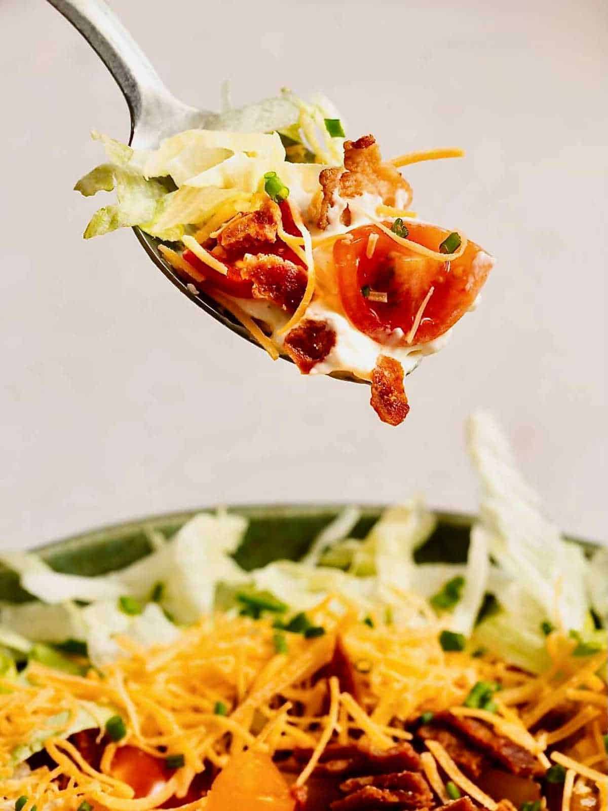 Spoon holding up a scoop of dip with bacon, lettuce and tomato on top.