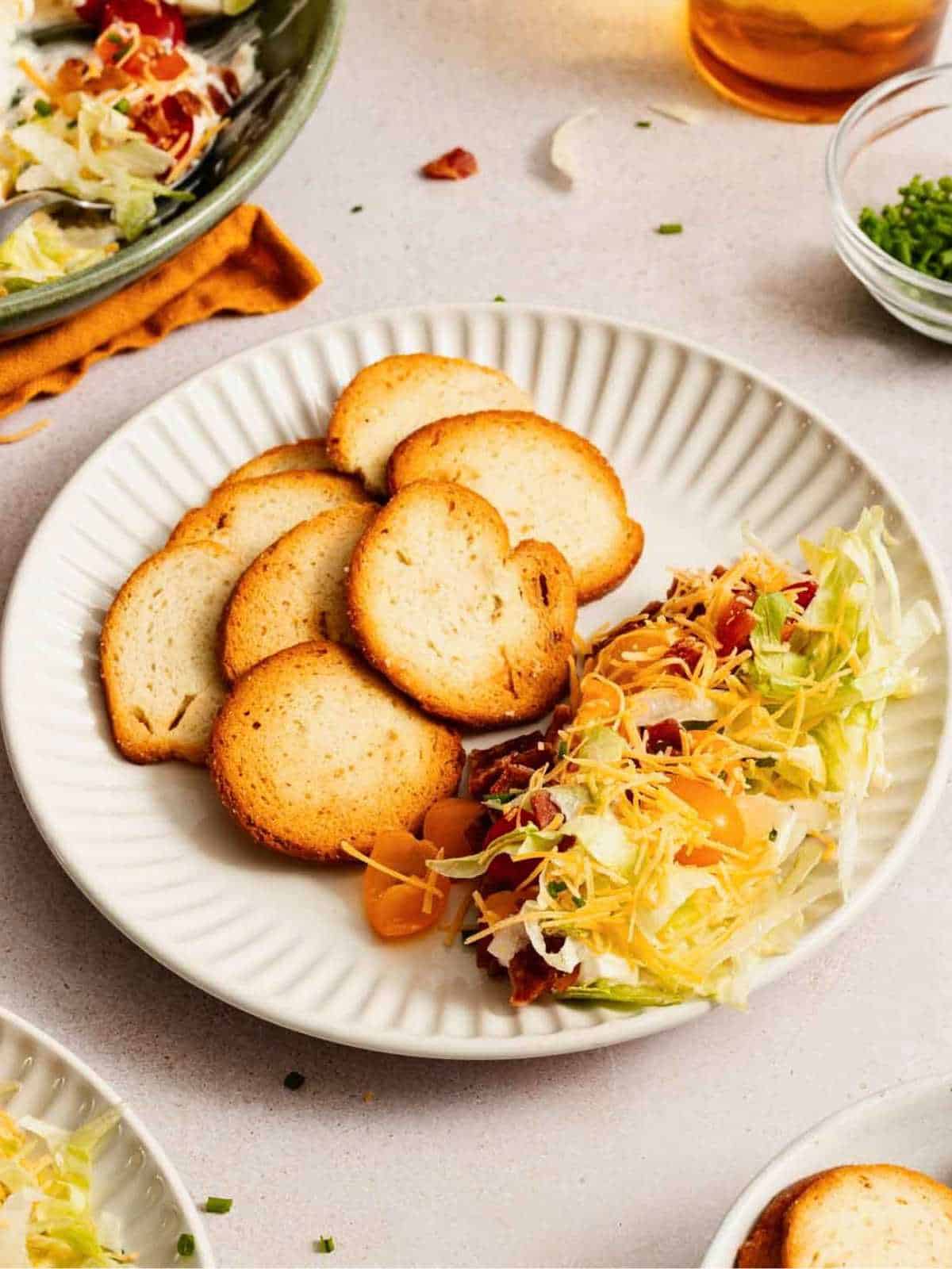 Lettuce, tomatoes and cheese with bagel chips on a white plate.