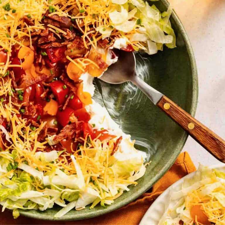 BLT Dip being scooped out of a green bowl with a wooden spoon.