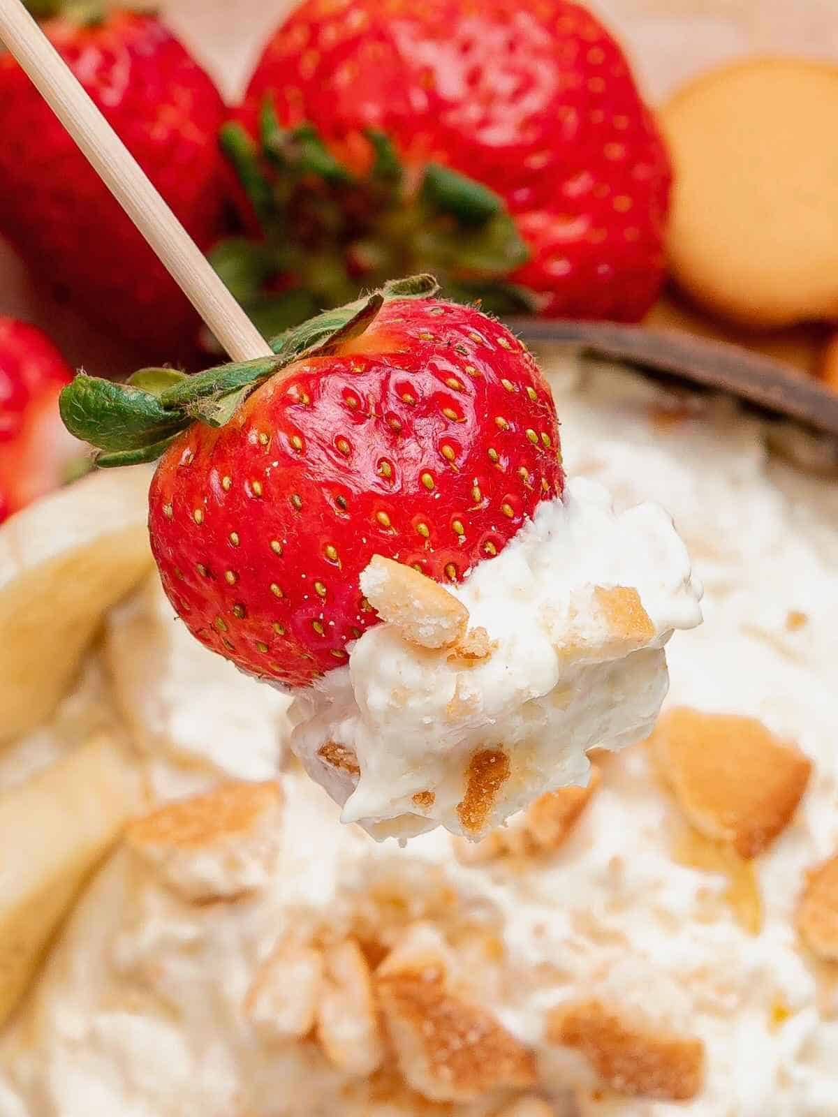 Fresh strawberry dipping into banana pudding dip with vanilla wafer crumbles.