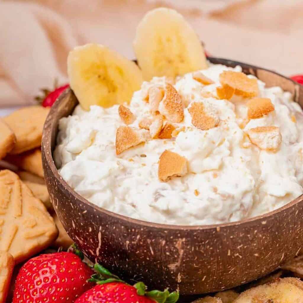 Banana slices top a bowl full of banana pudding dip sprinkled with vanilla wafer crumbles.