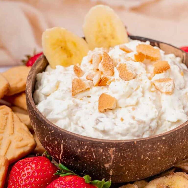 Banana slices top a bowl full of banana pudding dip sprinkled with vanilla wafer crumbles.