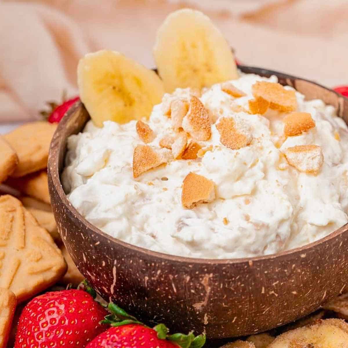 Banana slices top a bowl full of banana pudding dip sprinkled with vanilla wafer crumbles.