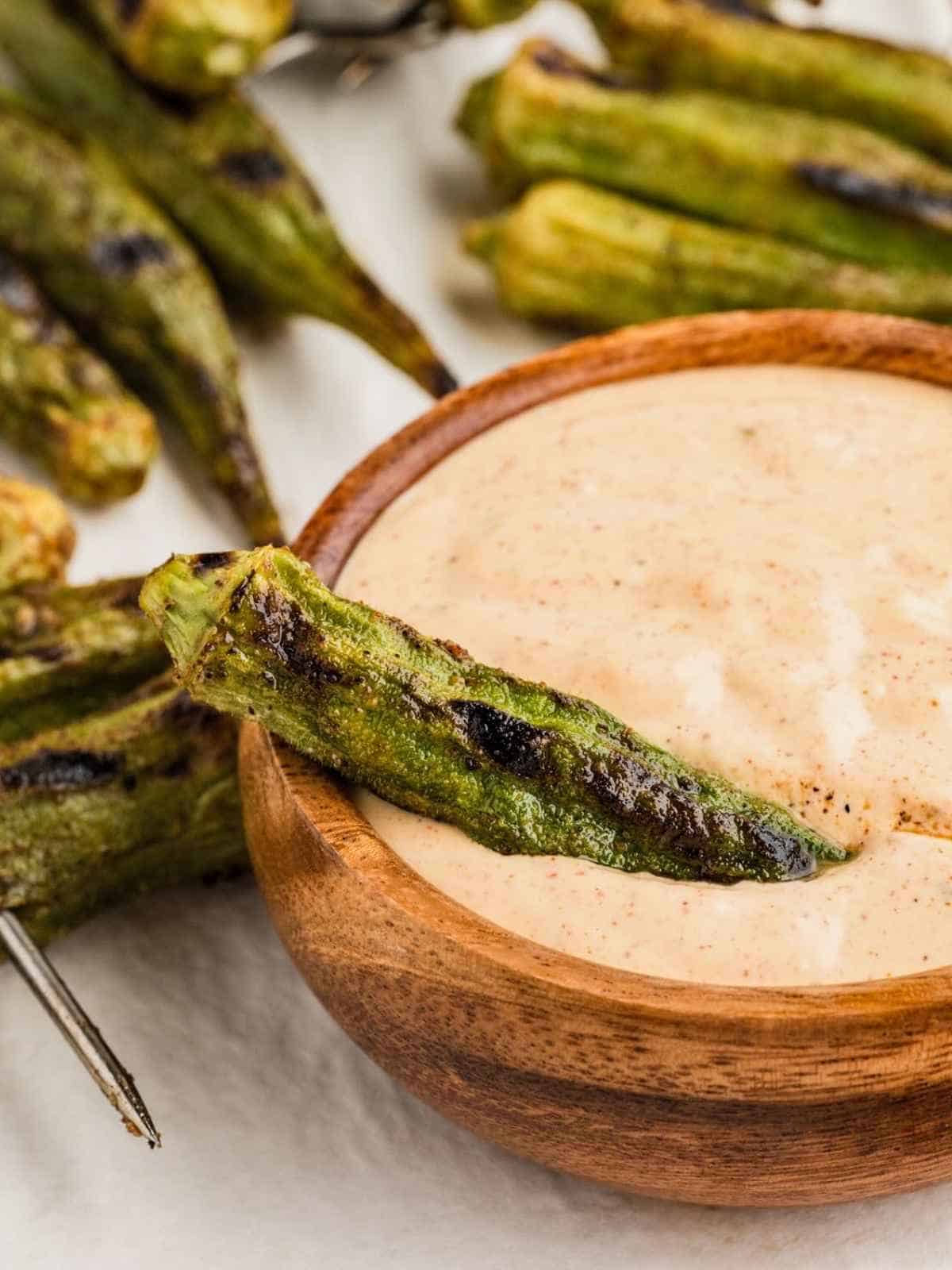 Grilled okra dipping into a bowl of Cajun dipping sauce.