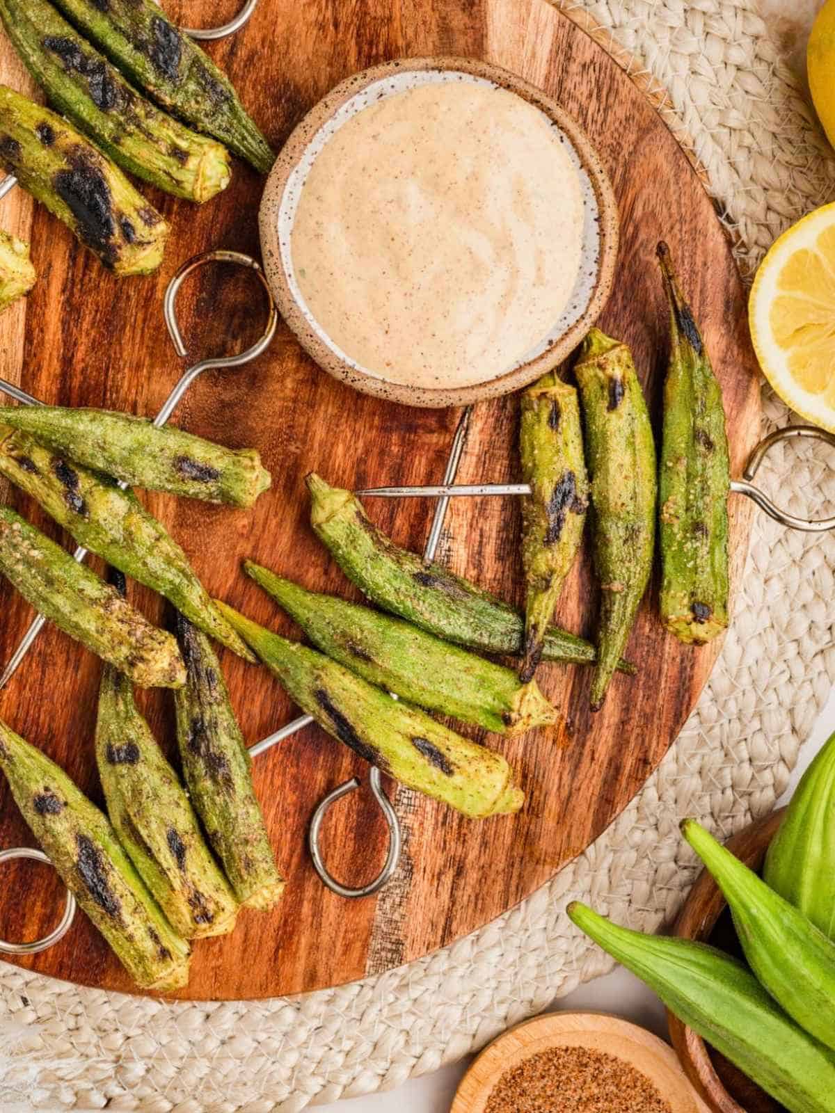 Cajun dipping sauce with grilled okra on skewers on a brown board.