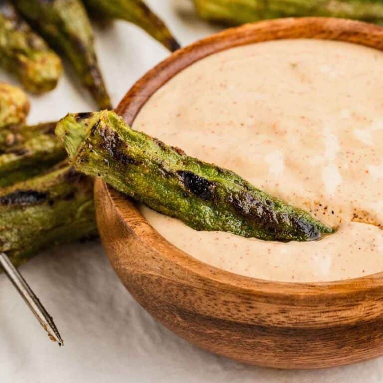 Grilled okra sitting on top of a brown bowl of Cajun Dipping Sauce.