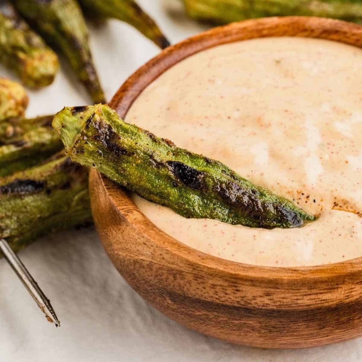 Grilled okra sitting on top of a brown bowl of Cajun Dipping Sauce.