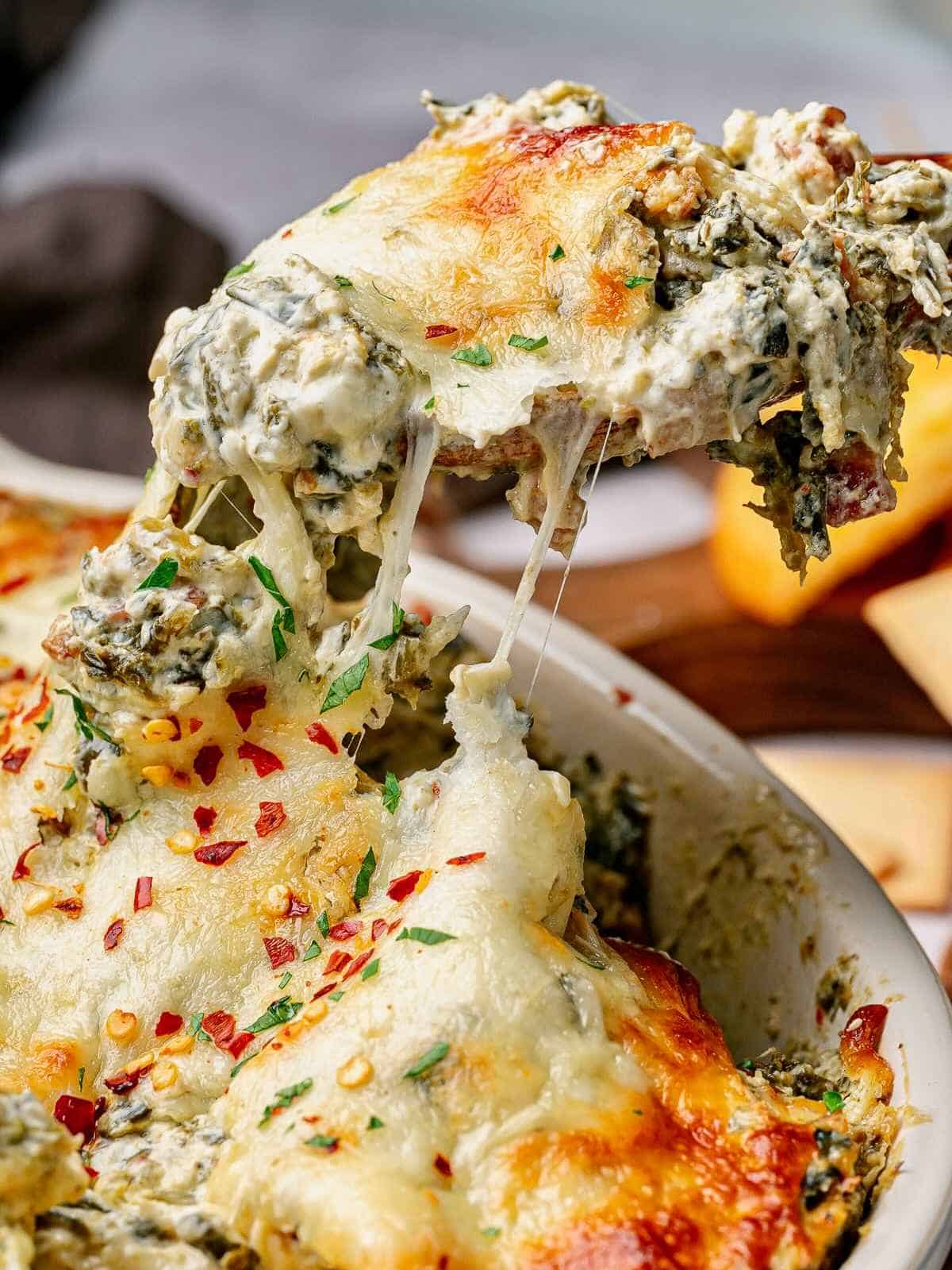 Spoon lifting up a scoop of collard greens dip over a baking dish.
