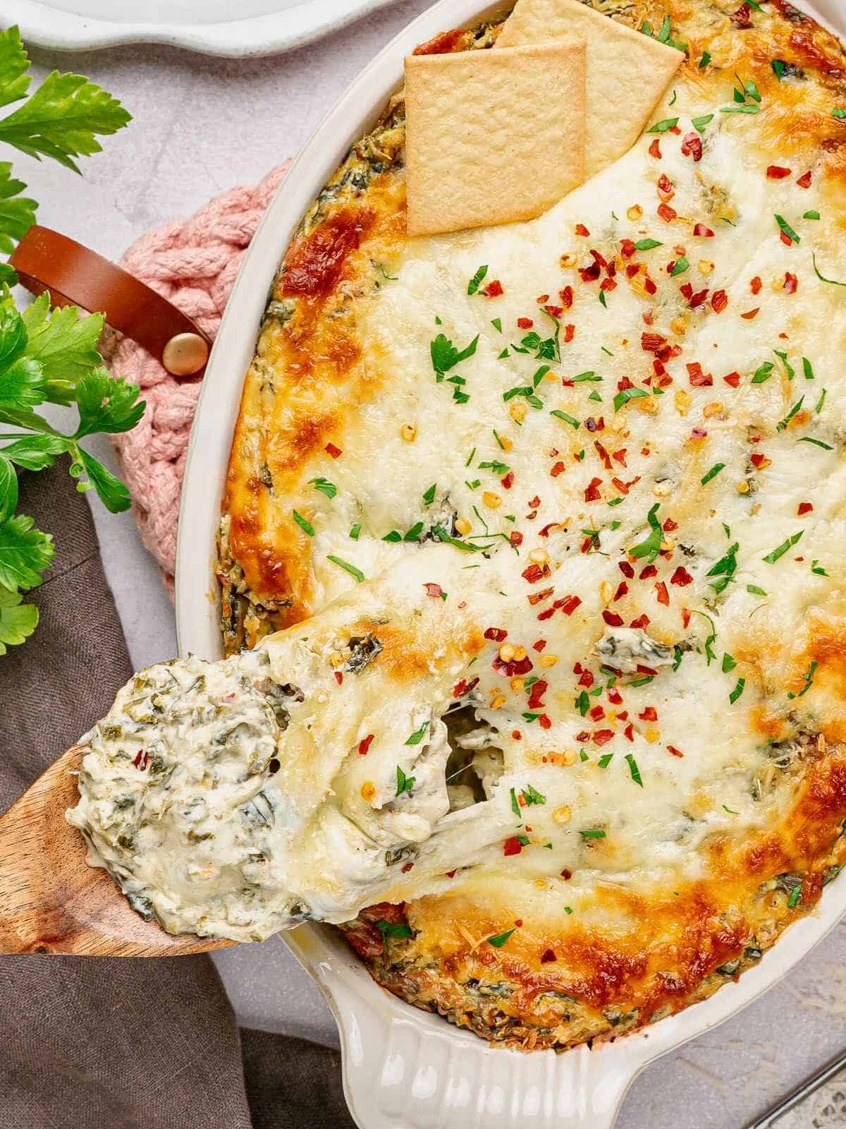 Collard greens dip coming out of the oven with a wooden spoon taking a big scoop.