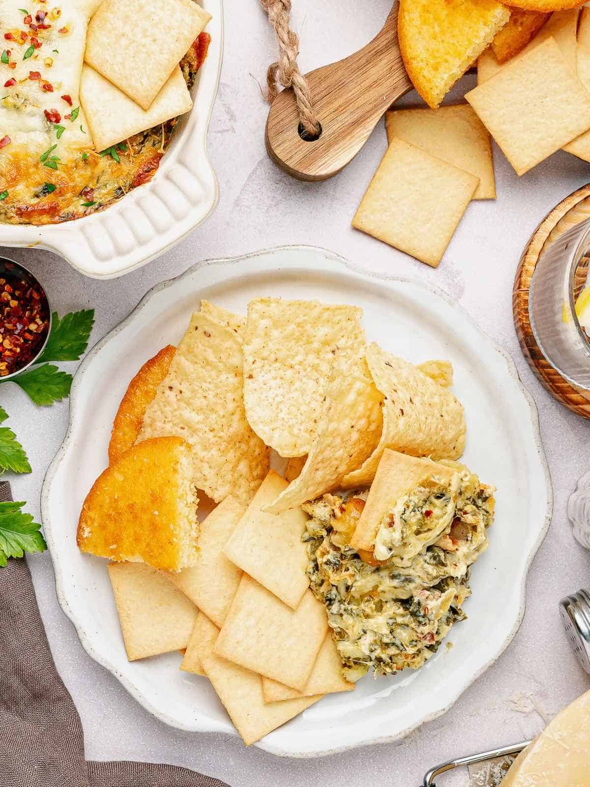 A white plate filled with tortilla chips, pita and cornbread with a side of dip.