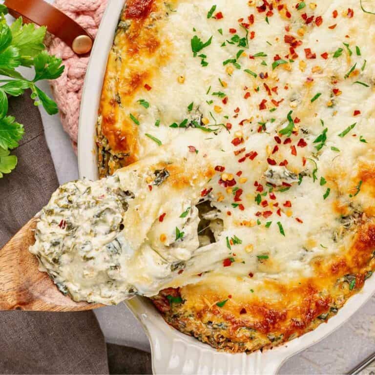 Wooden spoon dipping into a baking dish filled with cheesy Collard Greens Dip.