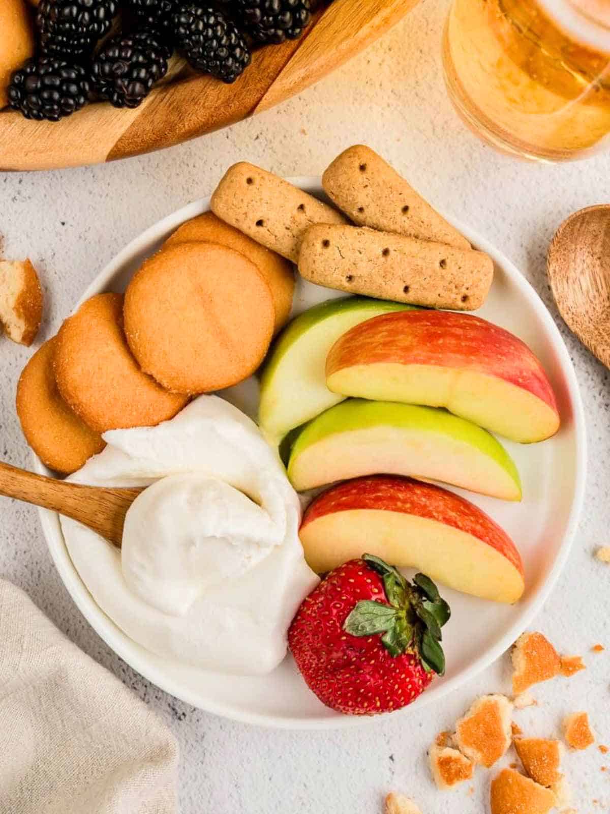 Serving of fruit dip with apples, vanilla wafers and a strawberry.