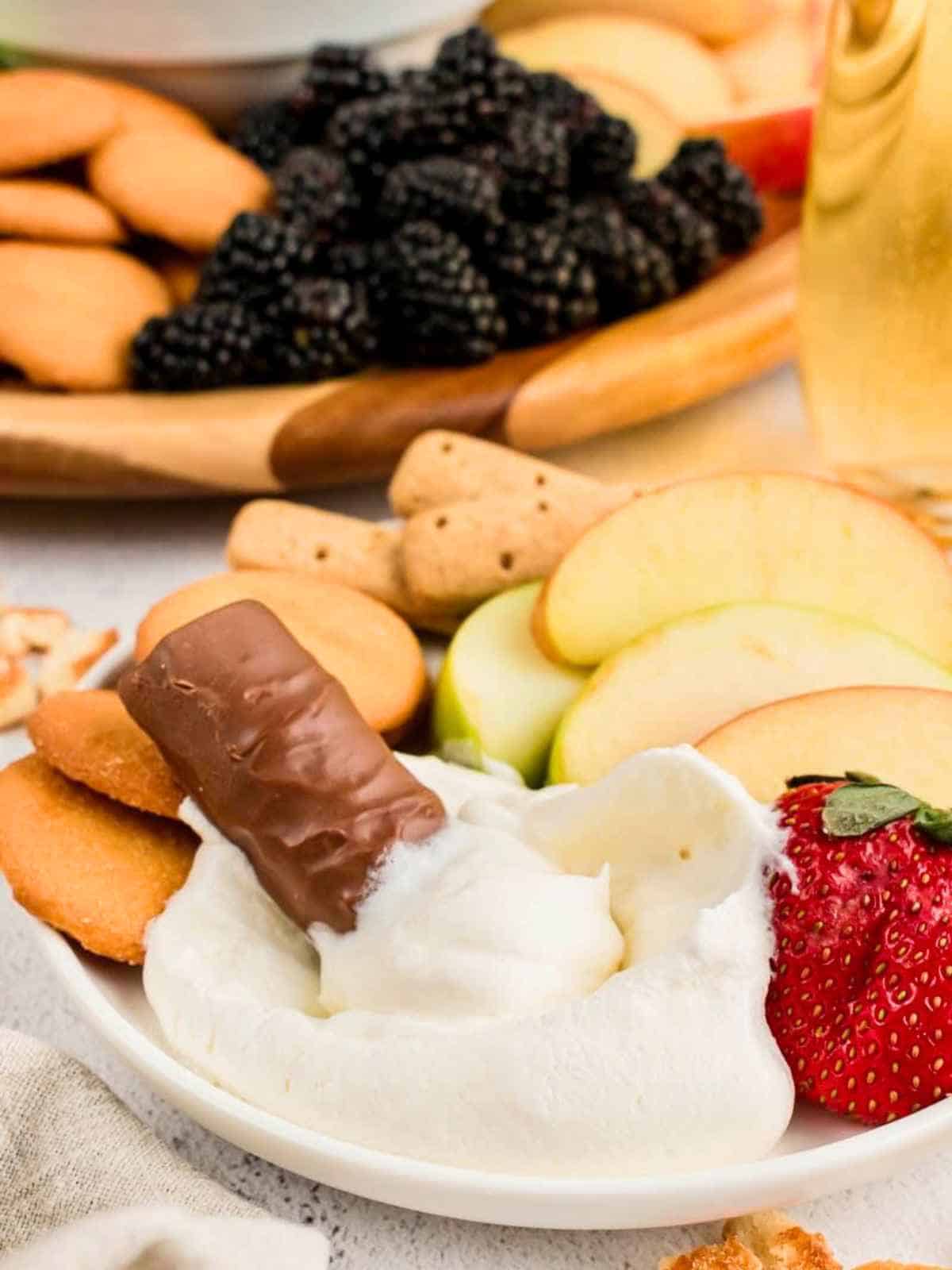 Twix candy bar dipping into cool whip fruit dip.