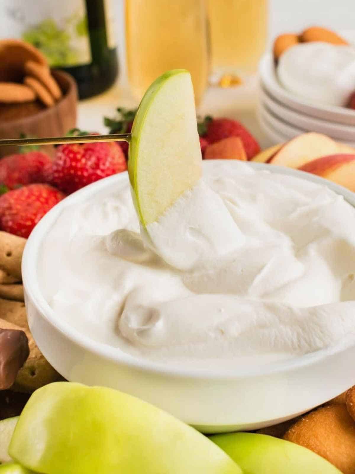 An apple slice dipping into cool whip fruit dip.
