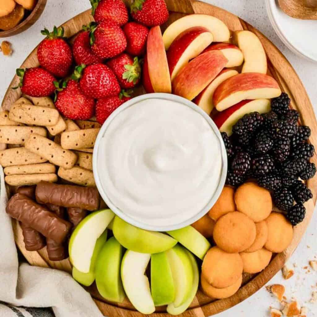 Cool Whip Fruit Dip in the middle of a dip board surrounded by fruit, cookies and candy.