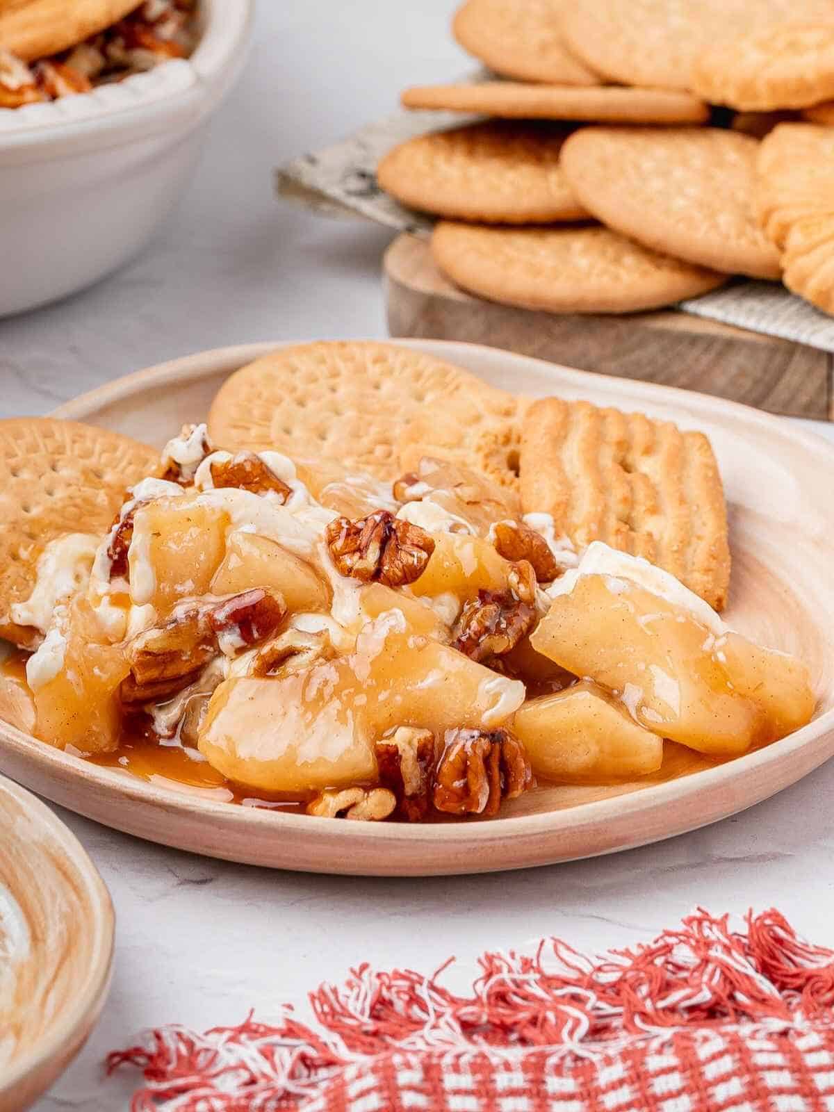 Serving of caramel apple dip with cookies on a beige plate.