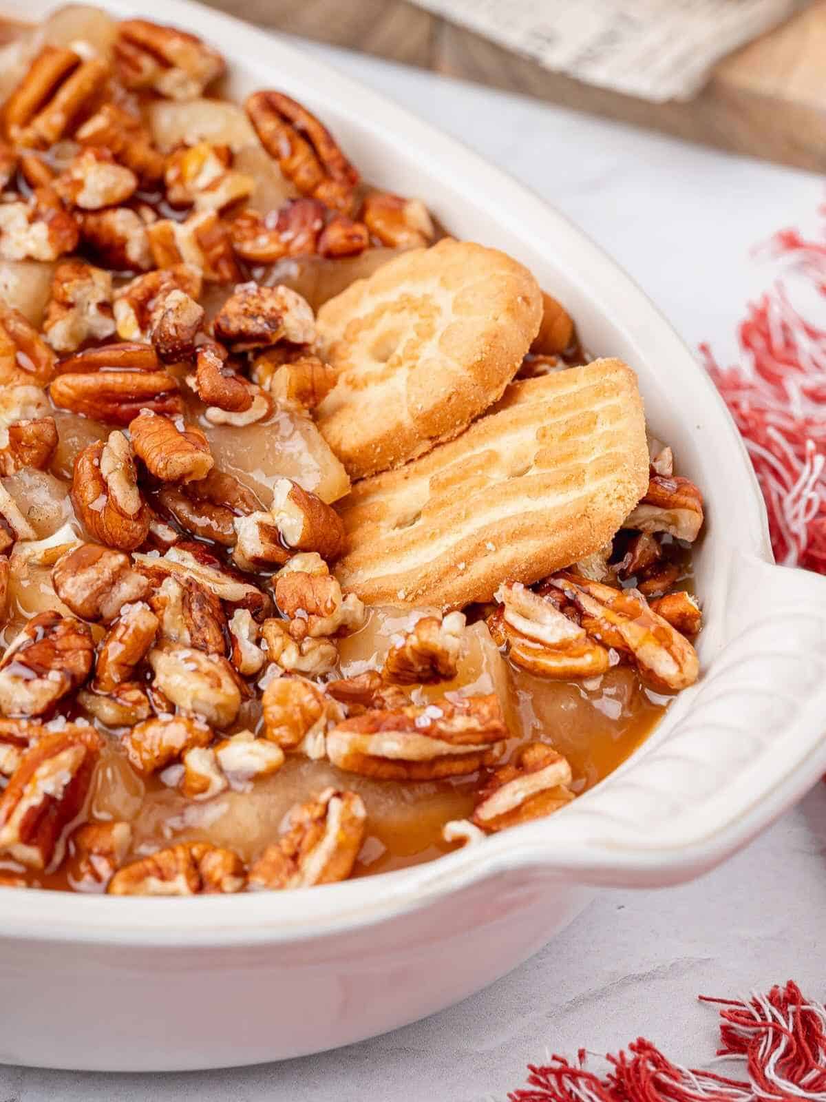 Pecans and caramel on top of cheesecake filling in a white baking dish.