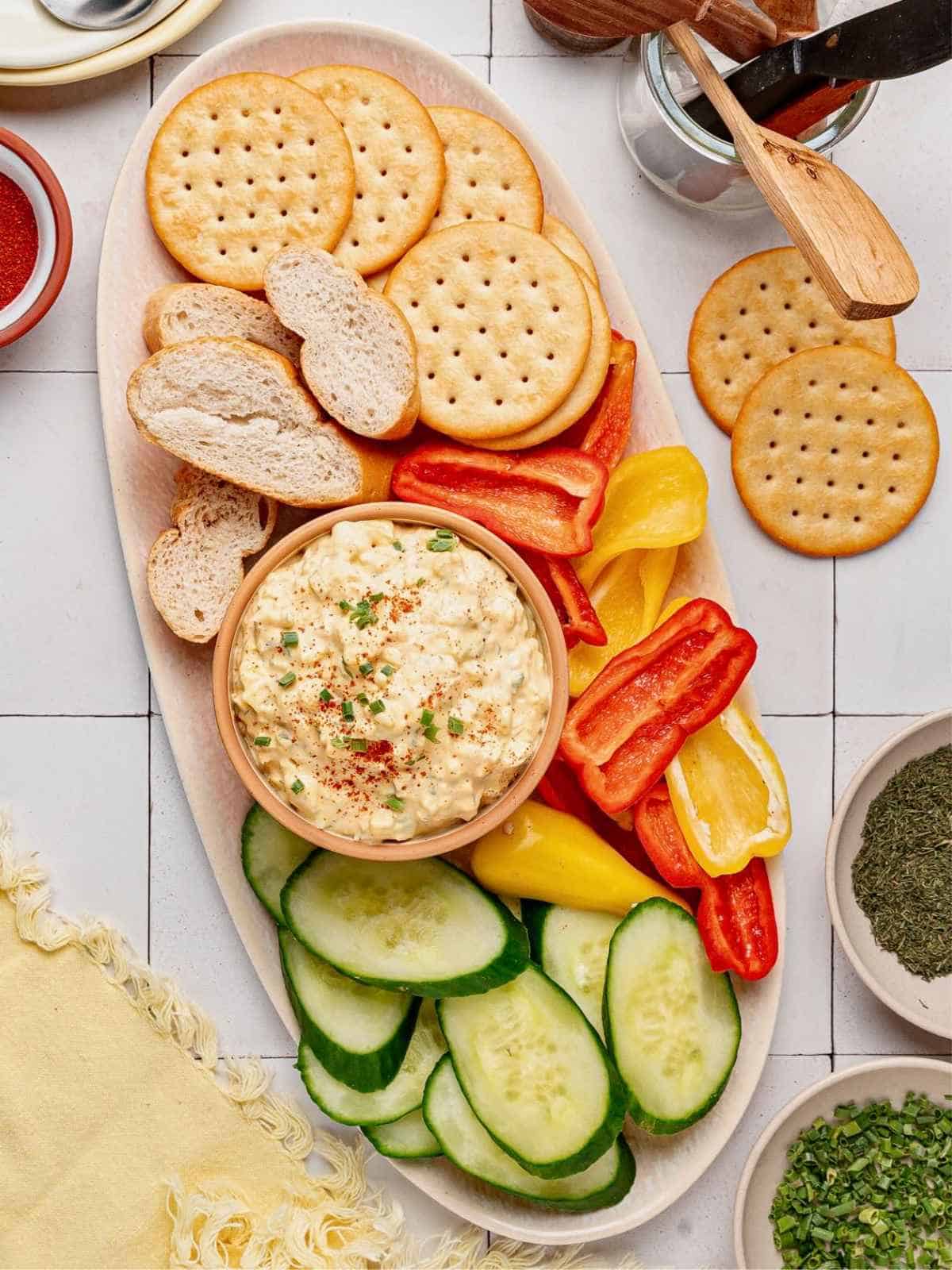 Deviled egg dip board surrounded by veggies and crackers.