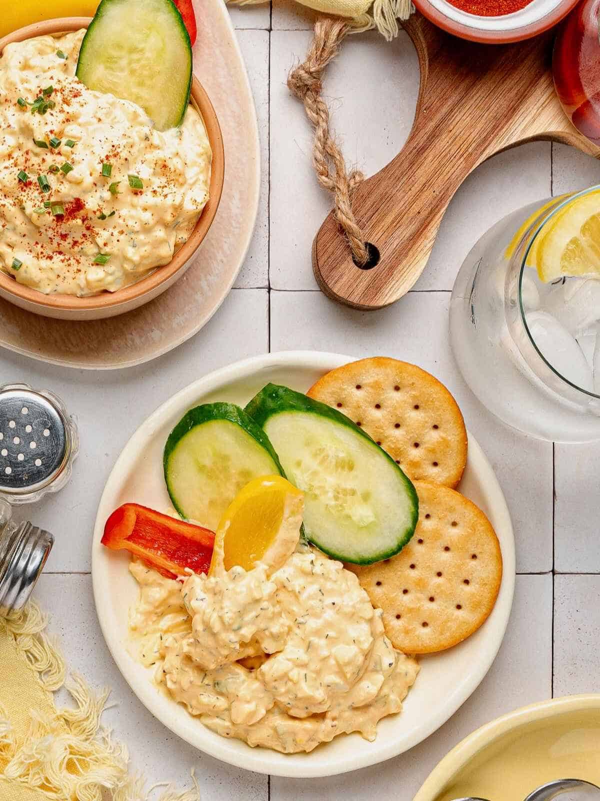 Humpty dumpty dip on a white plate with cucumbers, peppers and crackers.