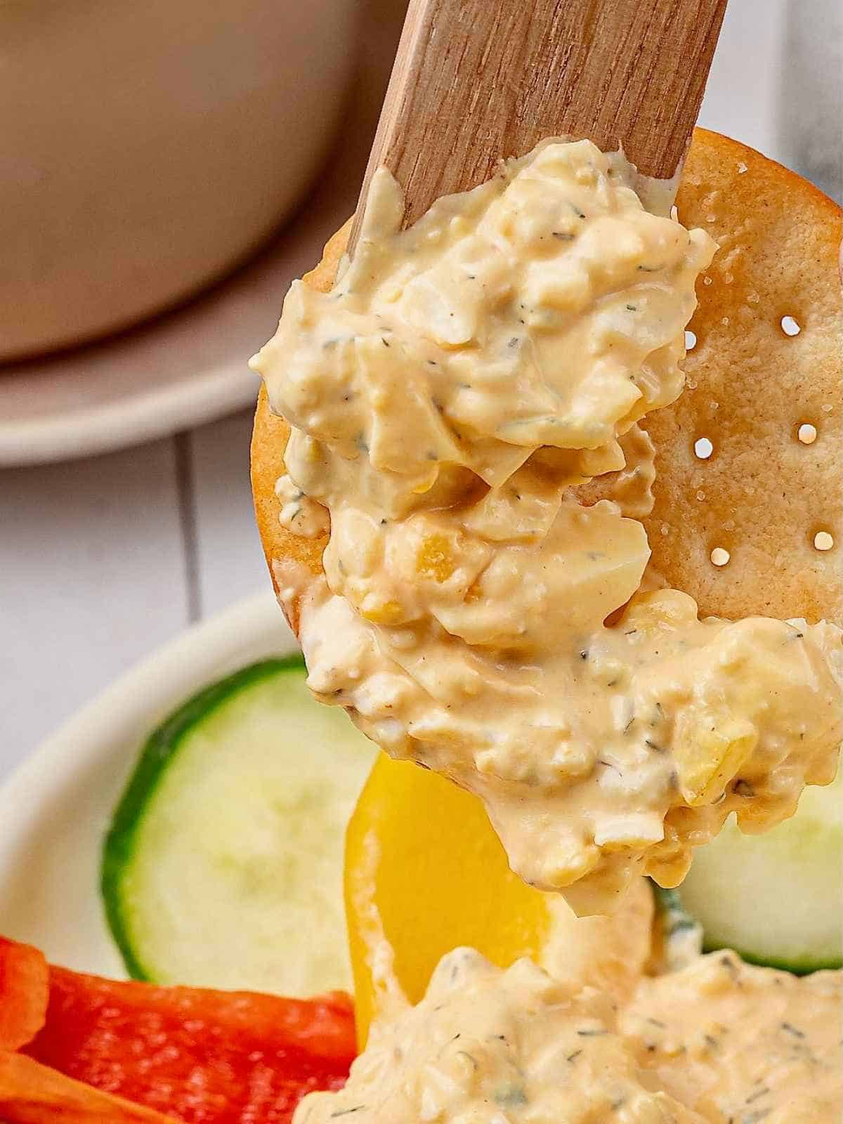 Wooden knife spreading dip on a cracker.