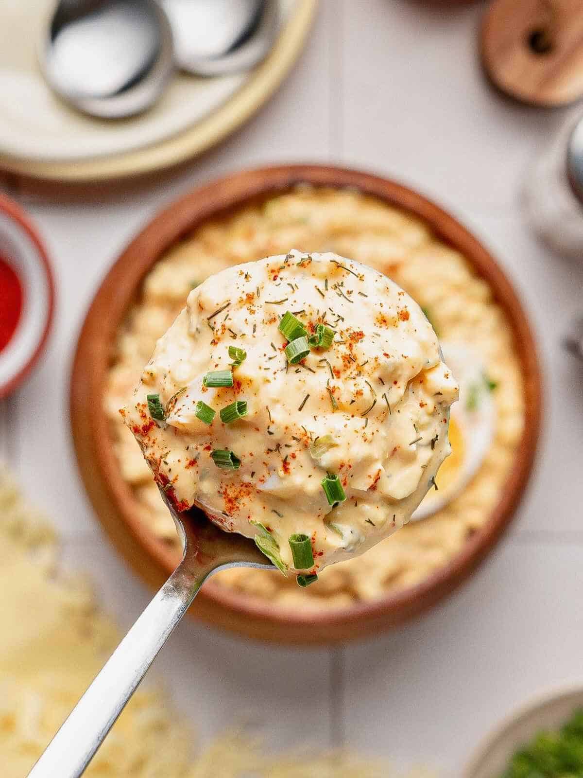 Deviled egg dip being lifted up by a spoon over a brown bowl.