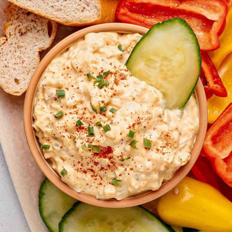 Cucumber slice dipping into a bowl of deviled egg dip, also called humpty dumpty dip.