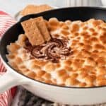 3-Ingredient S'mores Dip being swirled in a cast iron skillet with graham crackers.