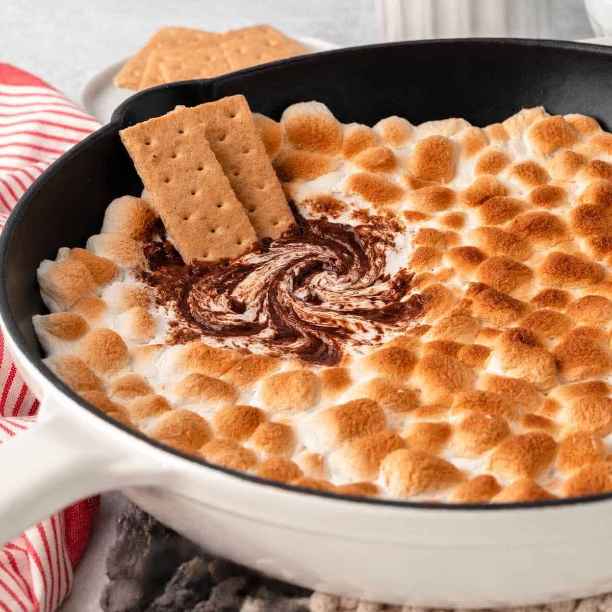 3-Ingredient S'mores Dip being swirled in a cast iron skillet with graham crackers.