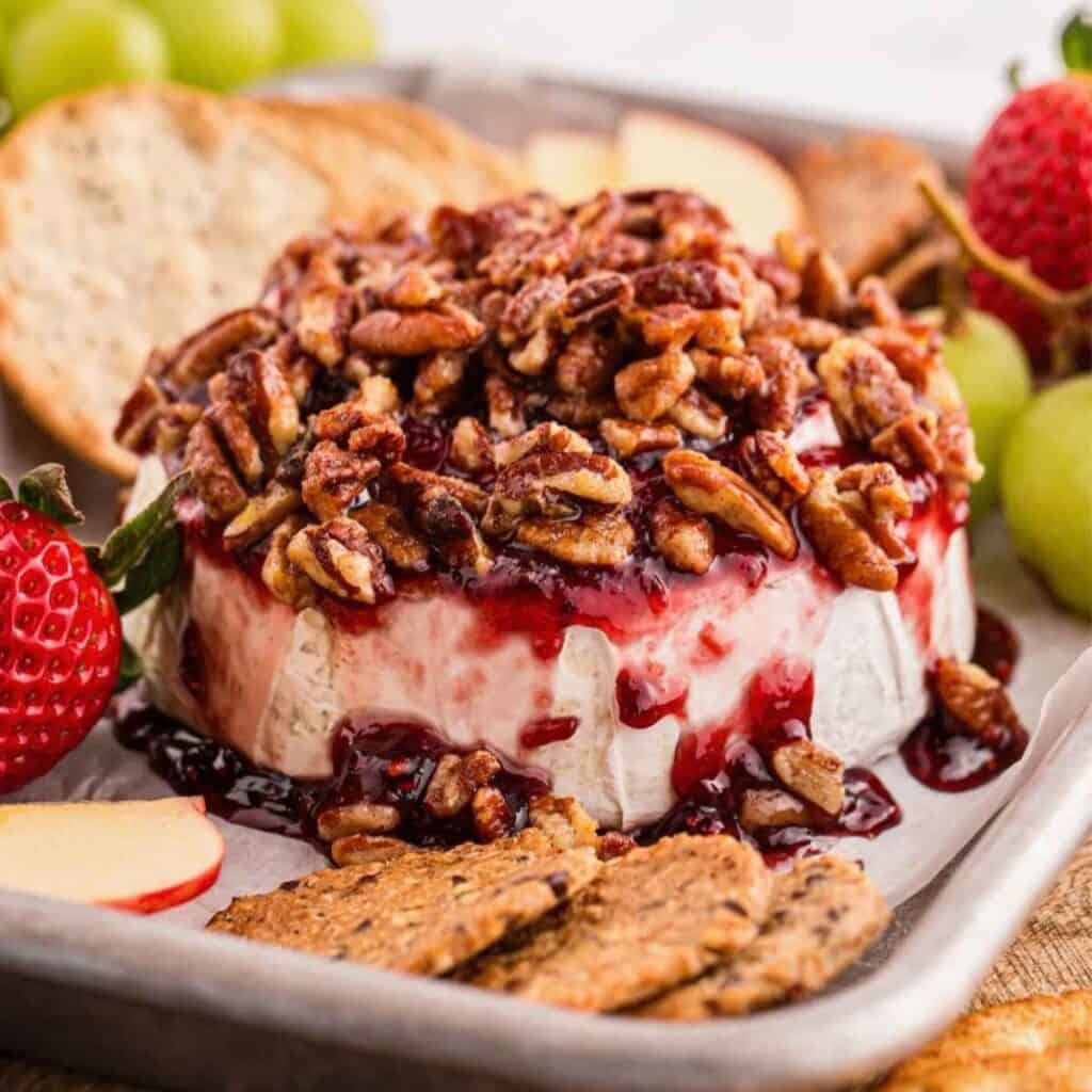 Baked Brie with Raspberry Jam on a board with fruit and crackers.