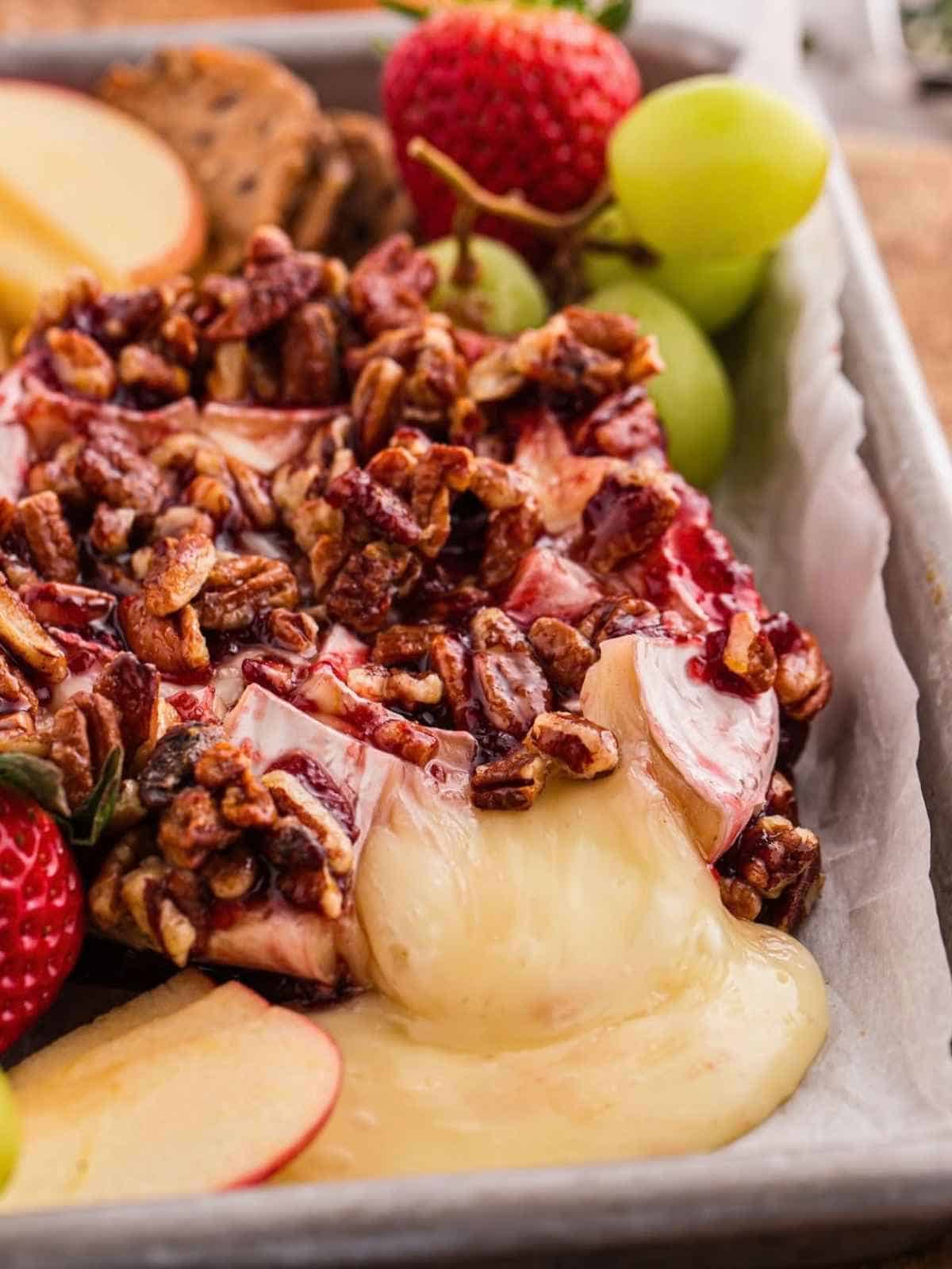 Baked Brie oozing out onto a sheet pan with pecans and raspberry jam.