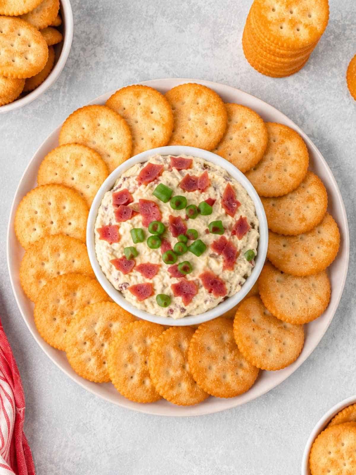 A white bowl of hot chipped beef dip with Ritz crackers.