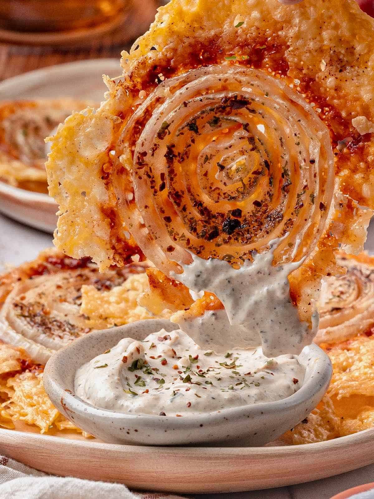 A large onion ring chip dipping into Garlic herb dip.