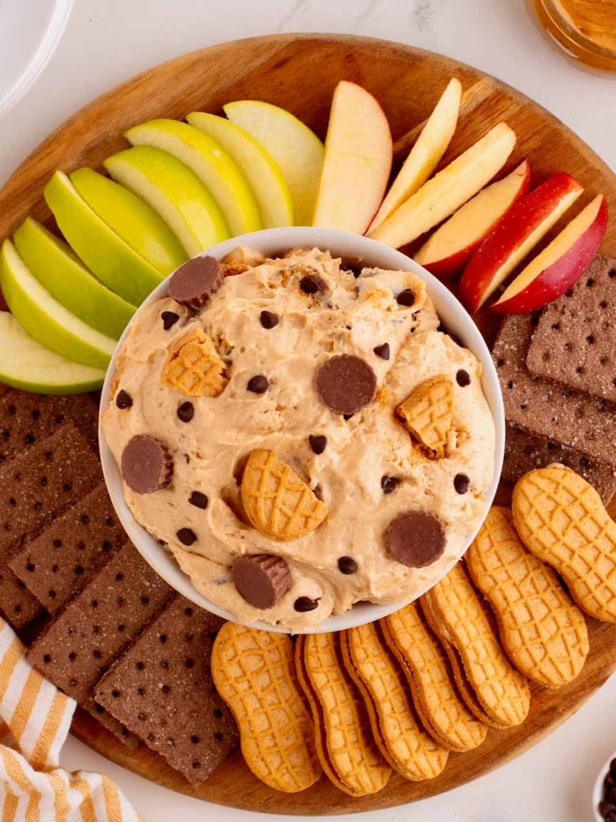 Platter of apples and cookies with peanut butter dip in the middle.