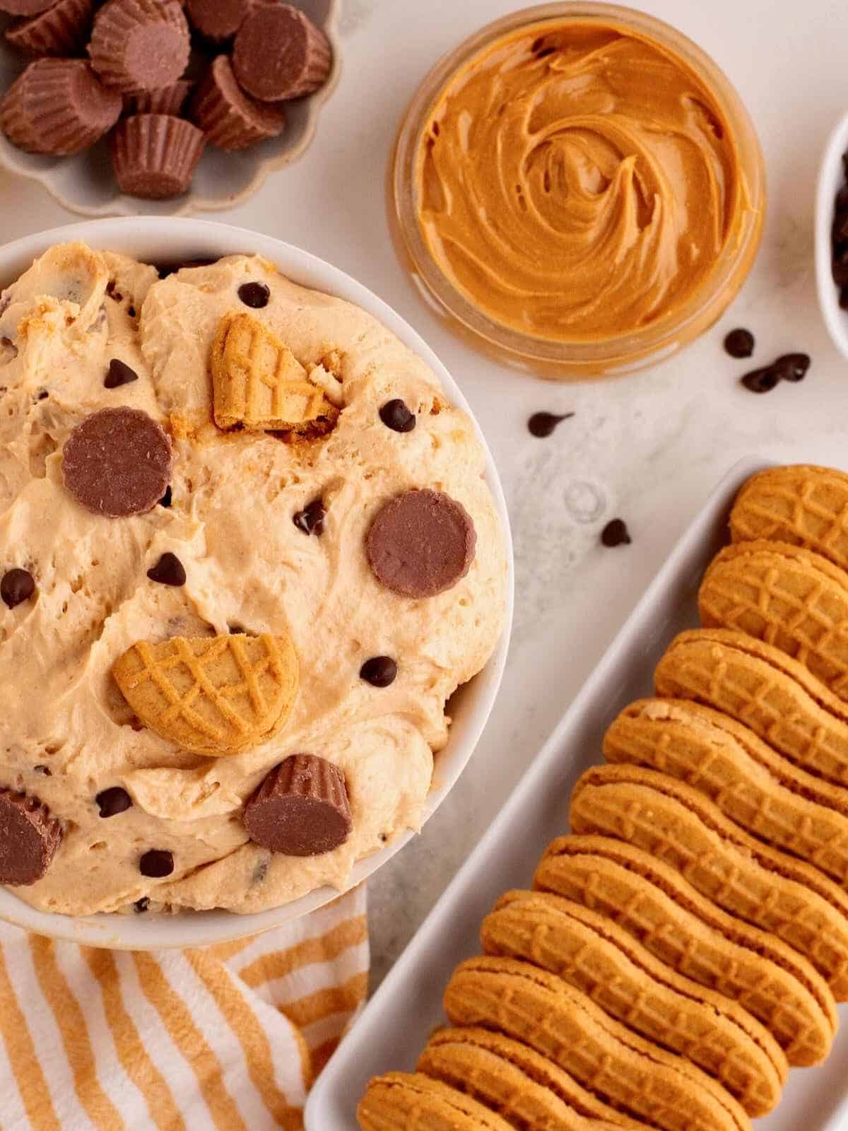 Peanut butter dip surrounded by a jar of peanut butter and cookies.