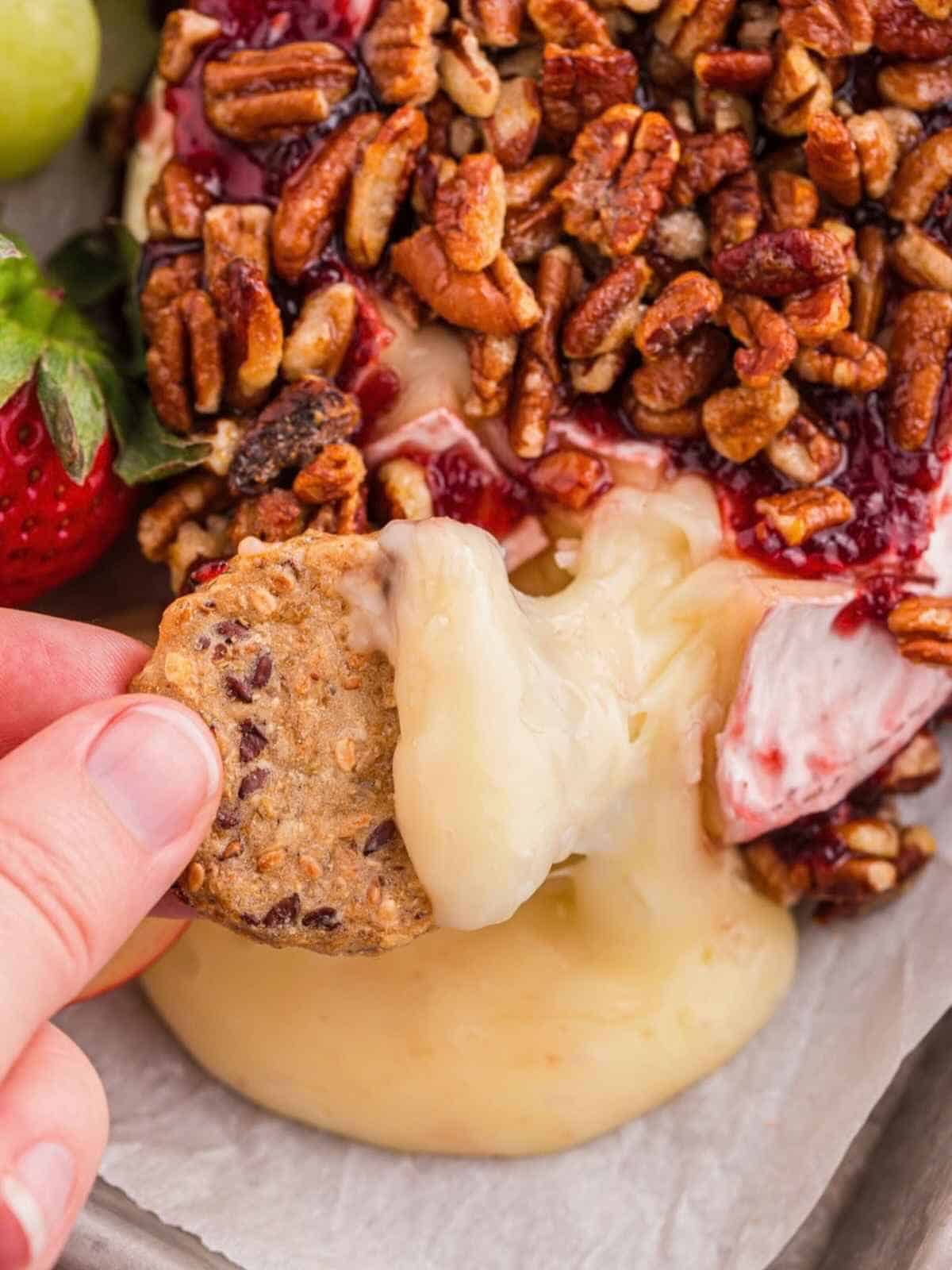 Scoop of brie with raspberry jam and pecans.