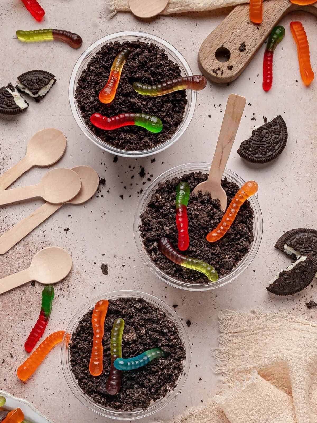 3 cups filled with Oreo cookie crumbs that look like dirt topped with gummy worms.