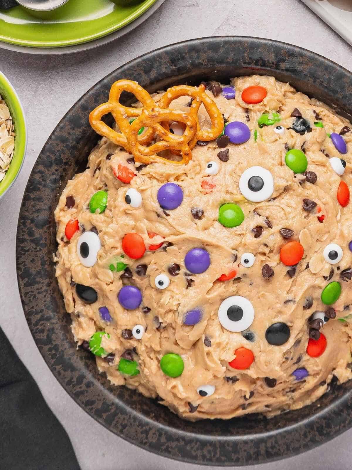 A bowl full of edible monster cookie dough with candy eyes and M&Ms.
