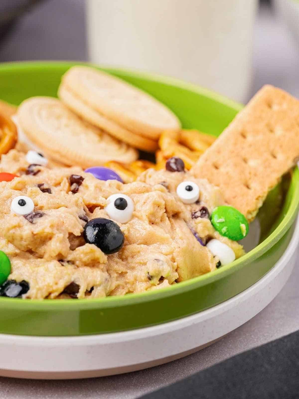 Monster cookie dough in a green bowl with graham crackers and cookies as dippers.